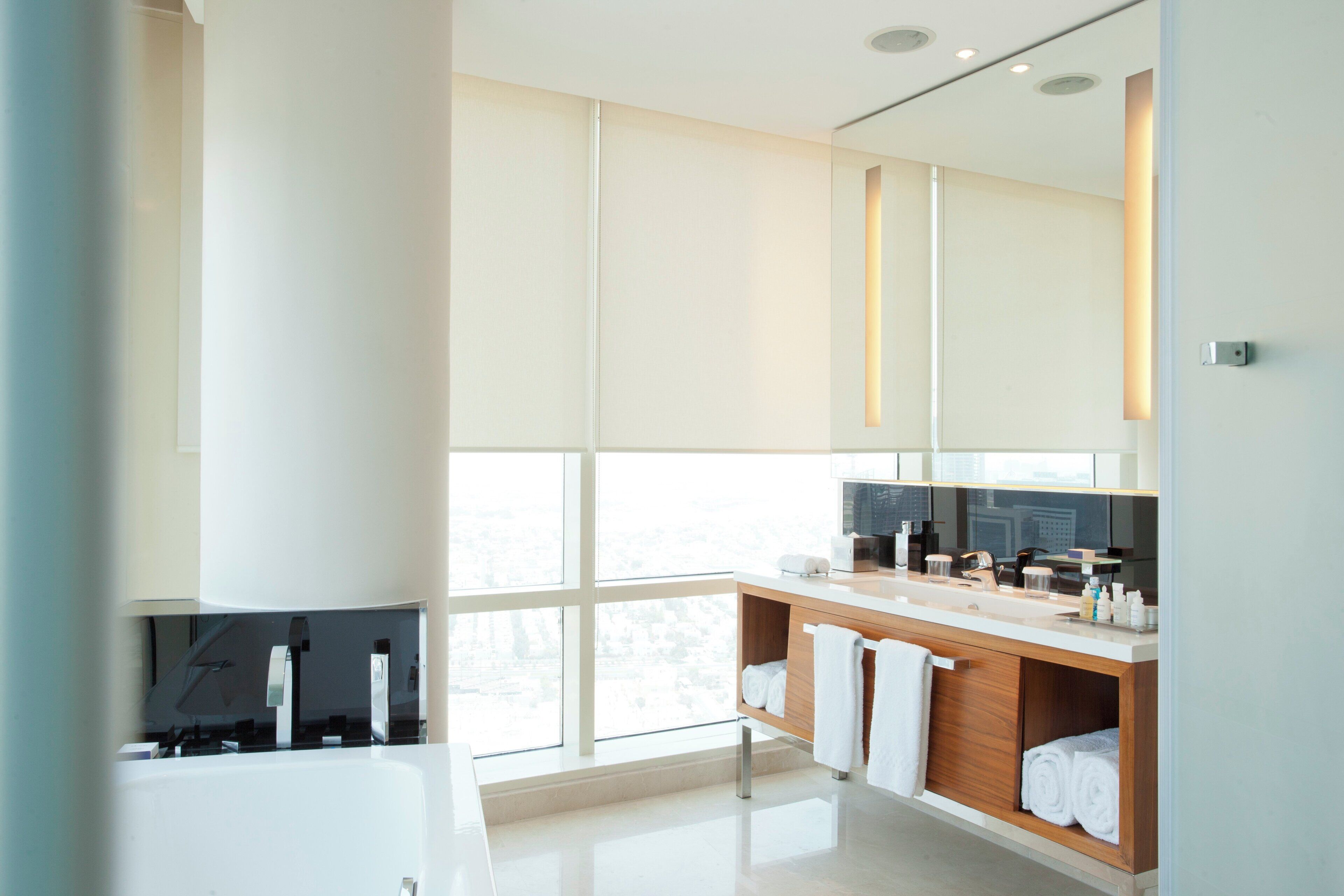 A modern bathroom with a large window, a bathtub, a vanity with a mirror, and a towel rack.