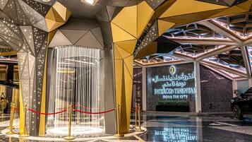 Une entrée moderne, avec un plafond au design géométrique, une fontaine et une enseigne indiquant « Intercontinental Doha The City ».