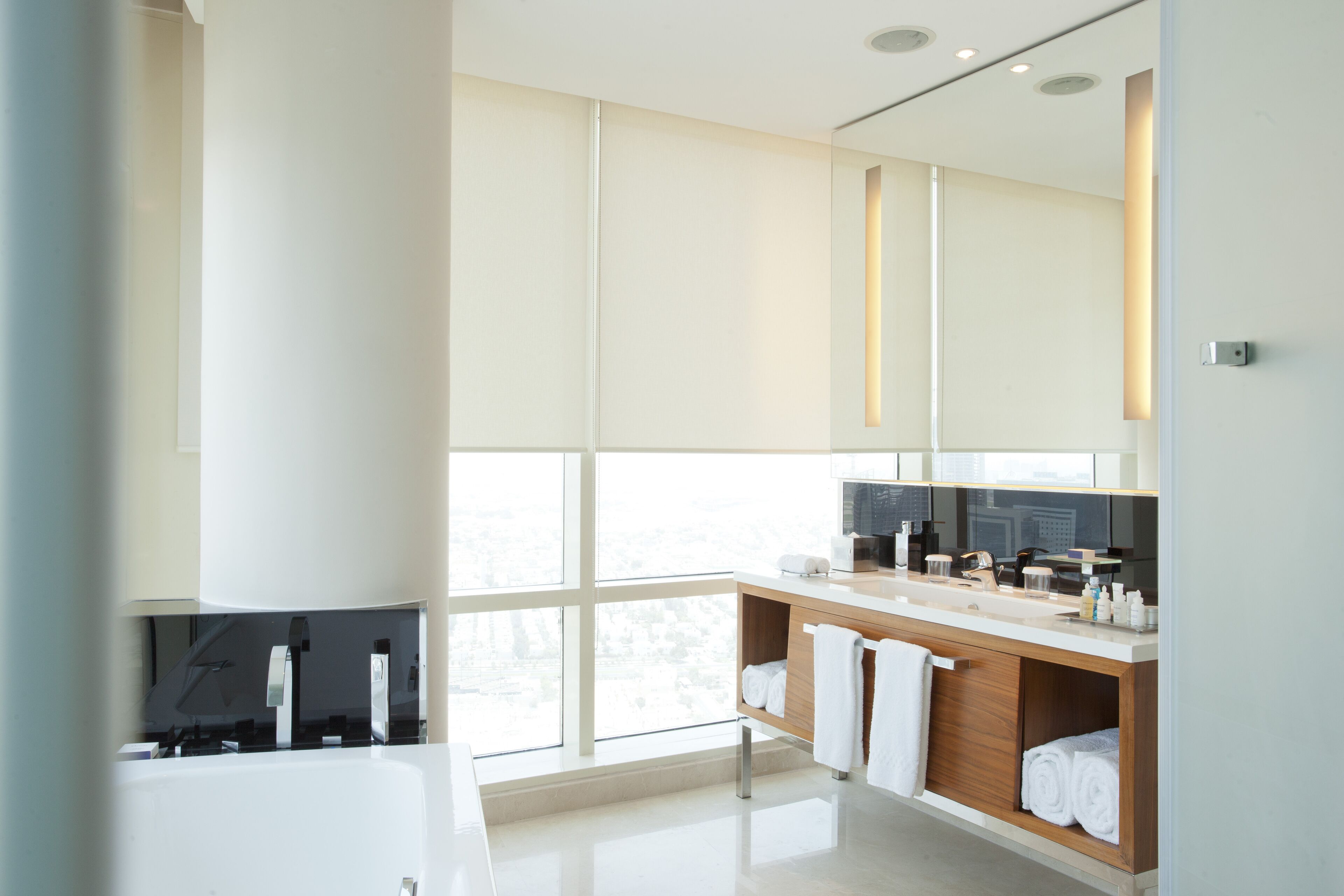Un baño moderno con un ventanal grande, una bañera, un tocador con espejo y toallas dobladas cuidadosamente.