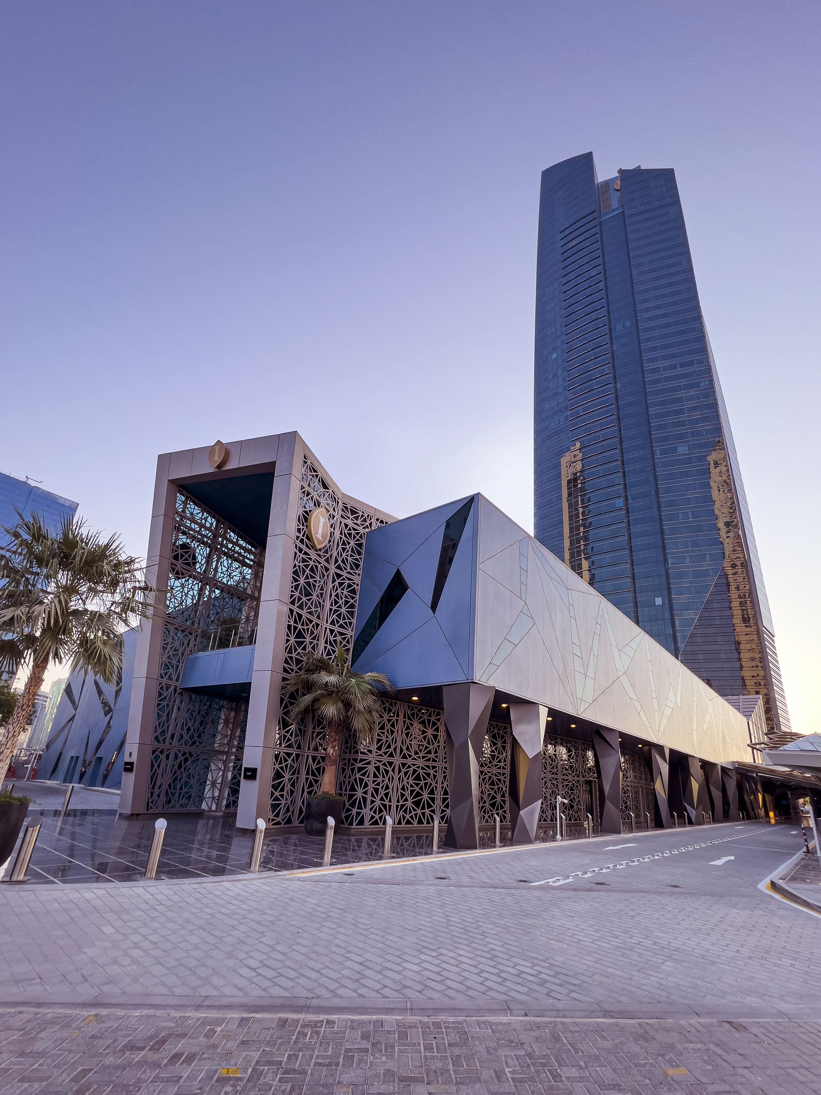 A modern building with a geometric facade and a tall skyscraper in the background.