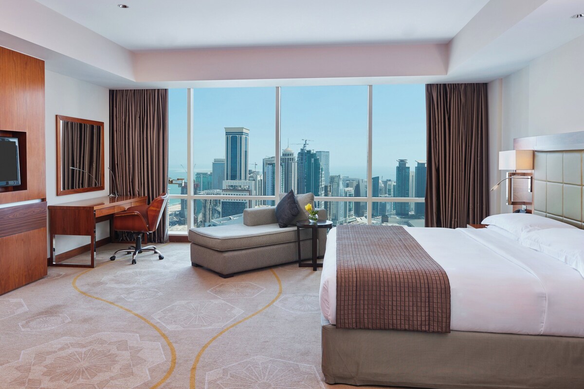 Habitación de hotel con vista a la ciudad, una cama, un escritorio, una silla y un televisor.
