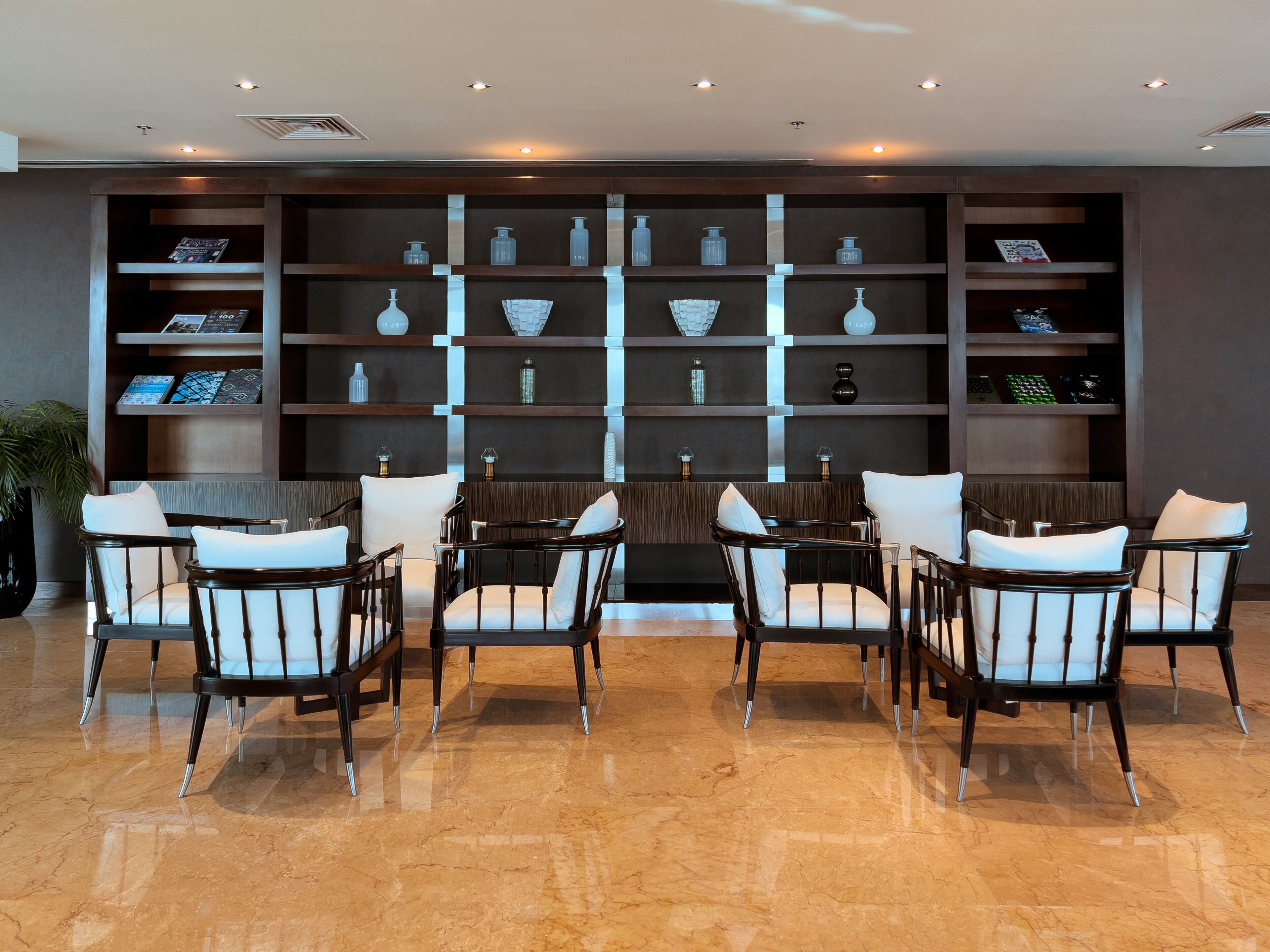A lobby with a seating area, marble flooring, and a wall with shelves displaying various items.