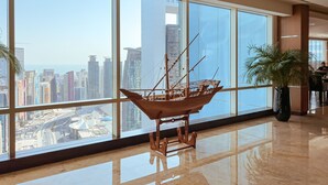 A spacious lobby with large windows offering a city view, a wooden ship model, and a potted plant. - InterContinental Doha The City by IHG (Doha)