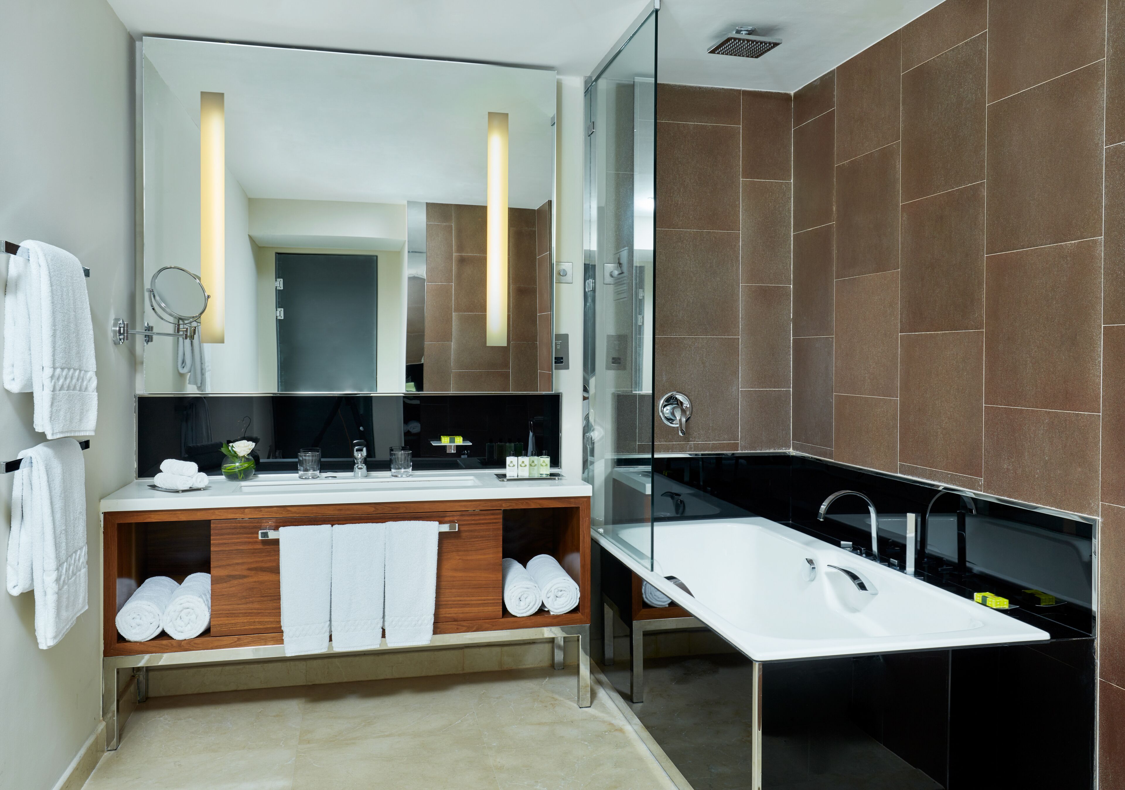 A modern bathroom with a large mirror, two sinks, a bathtub, and a wooden vanity.