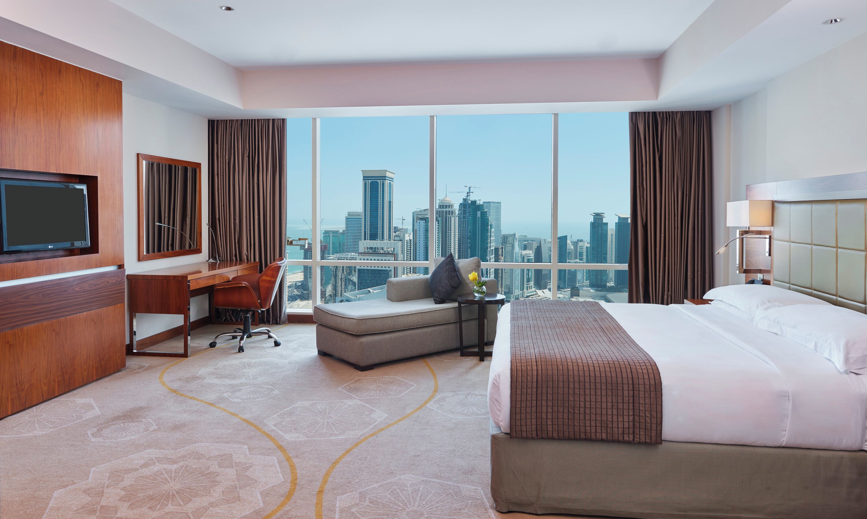 Une chambre d’hôtel avec un grand lit, un bureau, une chaise, une télévision, un canapé et une vue sur le panorama urbain.