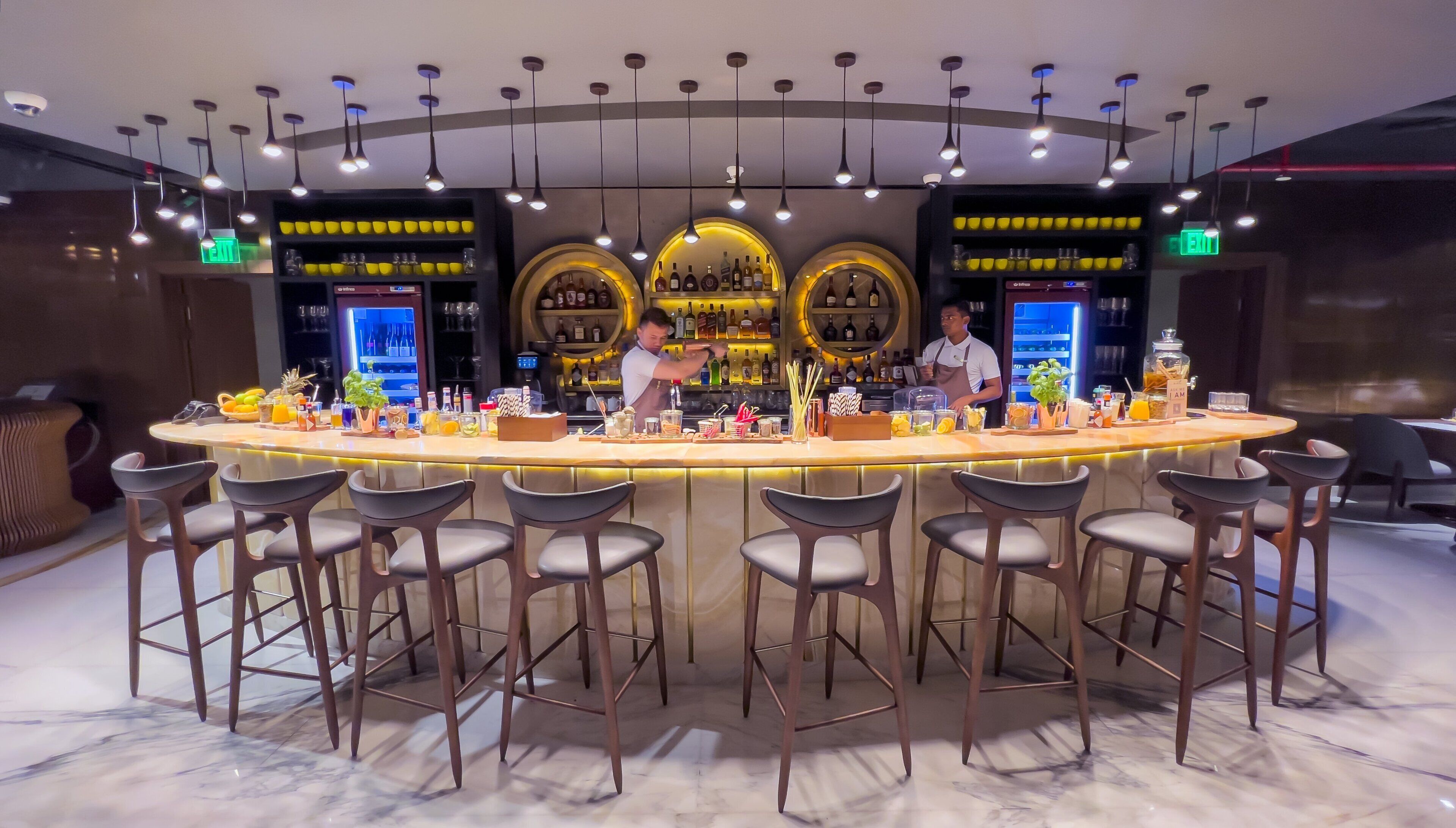 Zona de bar con suelo de mármol, varios taburetes y una barra repleta de botellas y vasos.
