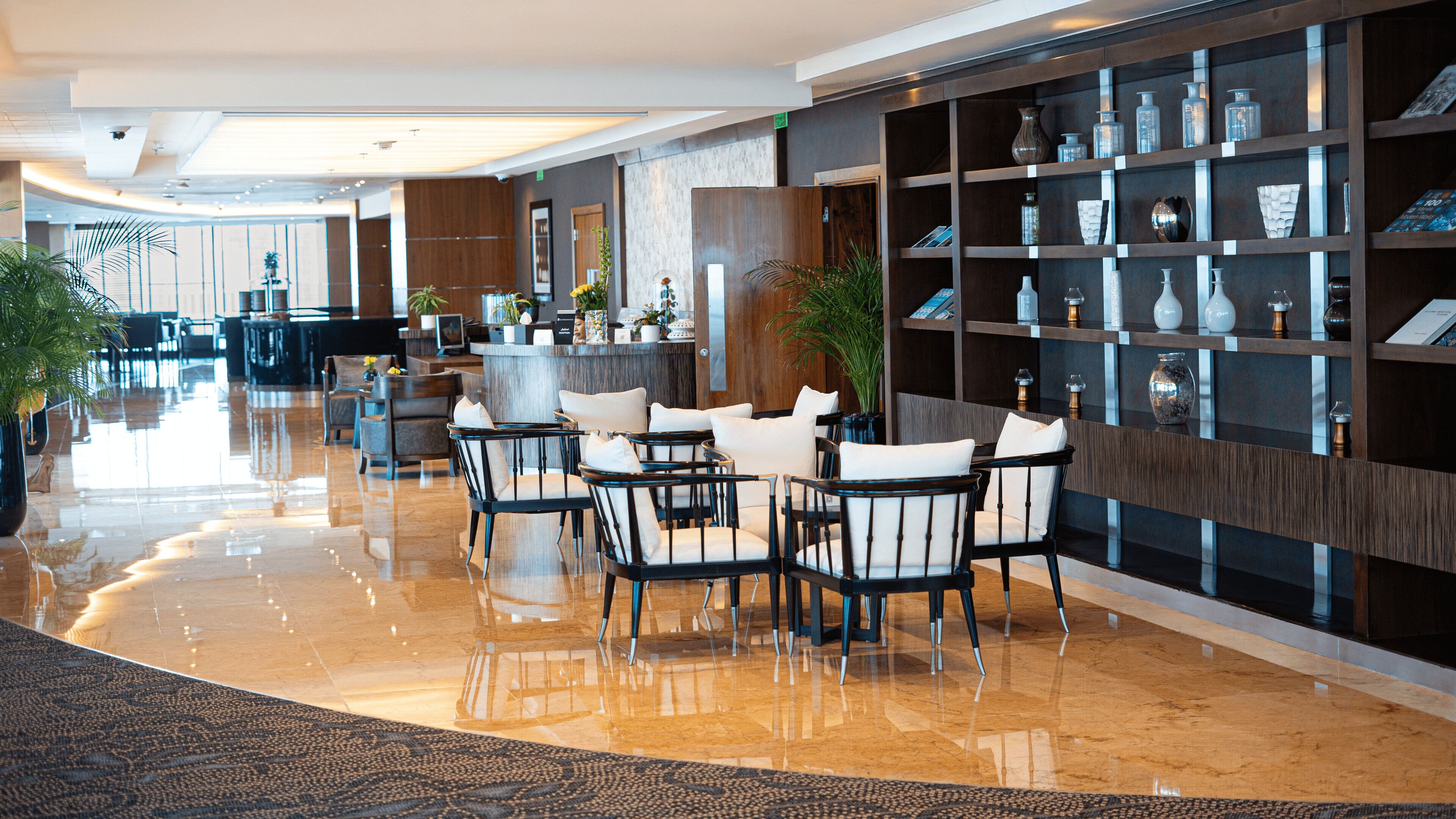A modern lobby with a polished marble floor, a reception desk, and a seating area with chairs and tables.