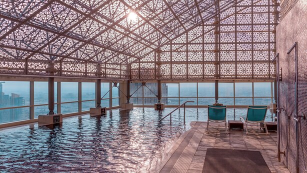 An indoor swimming pool with a geometric ceiling structure, clear windows, and seating areas. - InterContinental Doha The City by IHG (Doha)
