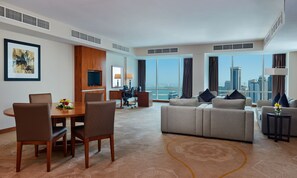 A modern hotel room with a dining area, a sofa set, a TV, and a city view.