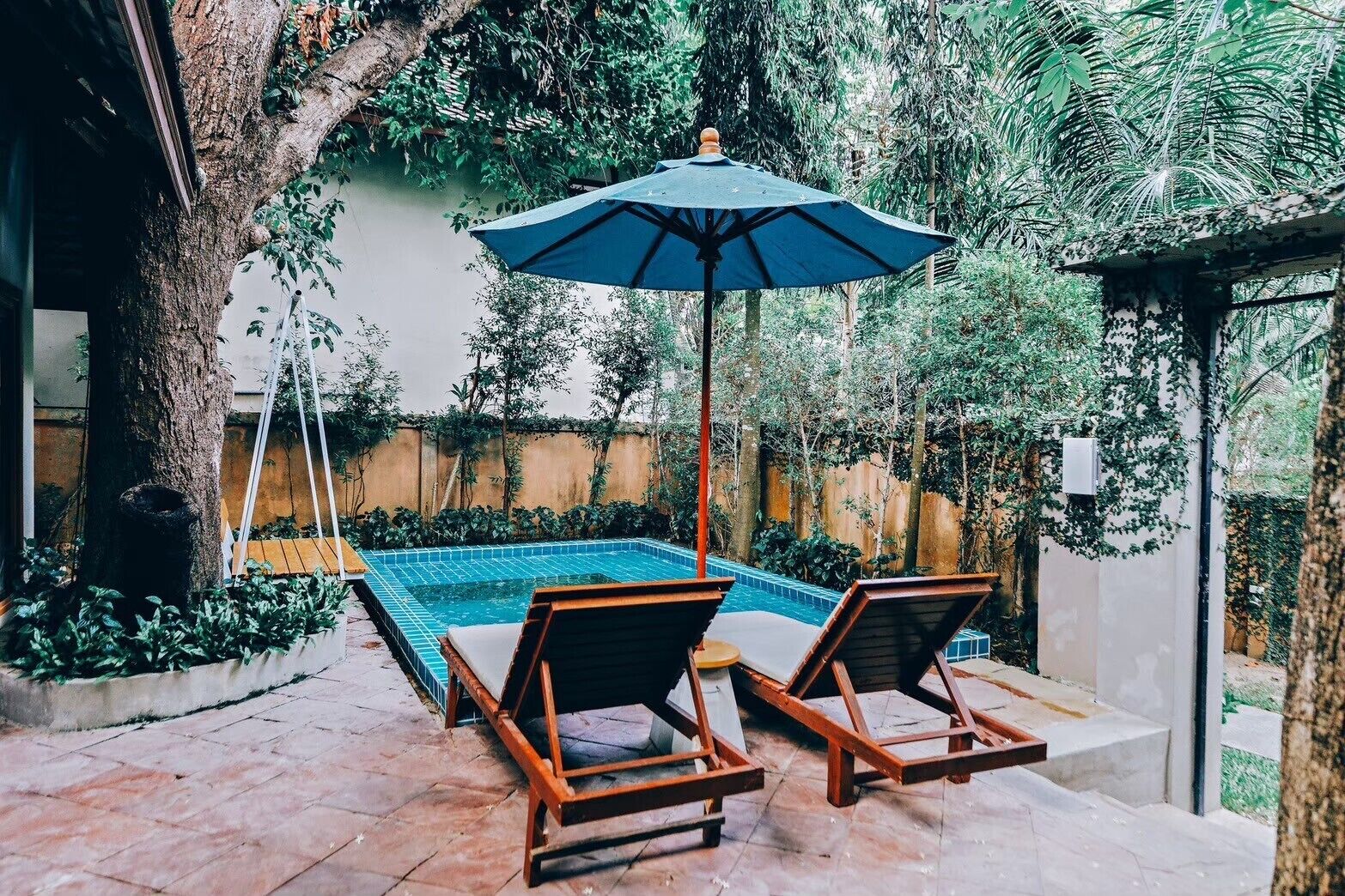 A swimming pool with two wooden lounge chairs and a blue umbrella.