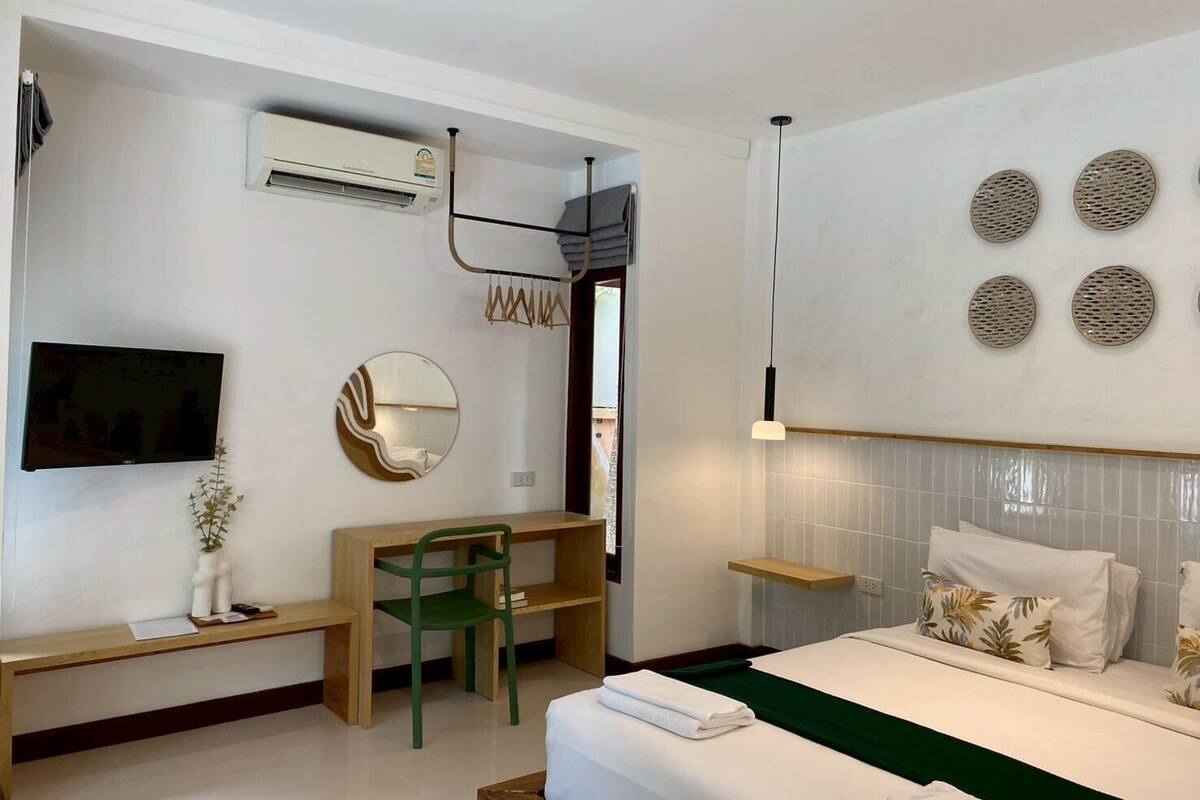 A modern hotel room with a bed, a desk, a chair, a TV, a mirror, and a wall-mounted air conditioner.