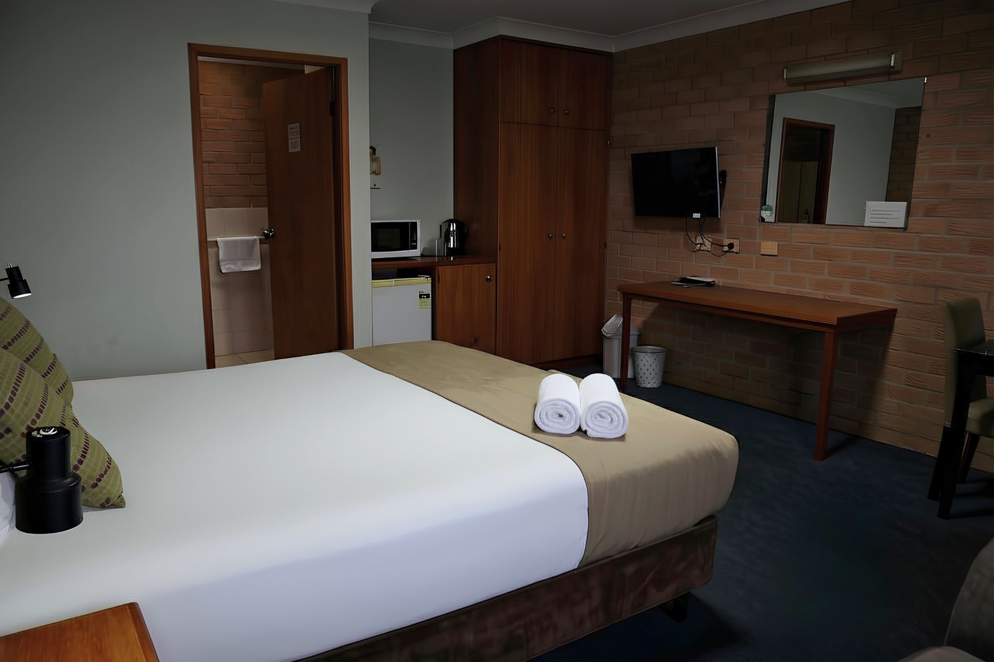 A hotel room with a bed, a desk, a mirror, a television, and a microwave.