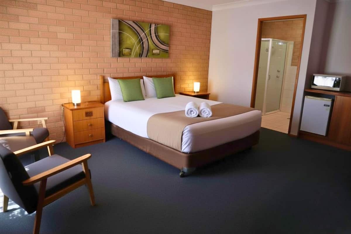 Ein Hotelzimmer mit einem Bett, einem Sessel, einem Nachttisch, einer Mikrowelle und einer Dusche.