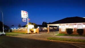 Ein Motel mit Ziegelbau, gut beleuchtetem Eingang und einem Schild, das Zimmer und Annehmlichkeiten bewirbt.