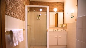 Ein Badezimmer mit einer gläsernen Duschkabine, weißen Fliesen, einem Waschbecken mit Spiegel und einem Handtuchhalter.