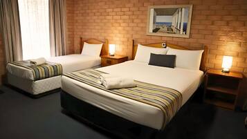 A hotel room with two beds, a brick wall, a window with curtains, and a painting.