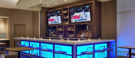 A bar area with a central counter, multiple stools, and shelves with bottles.