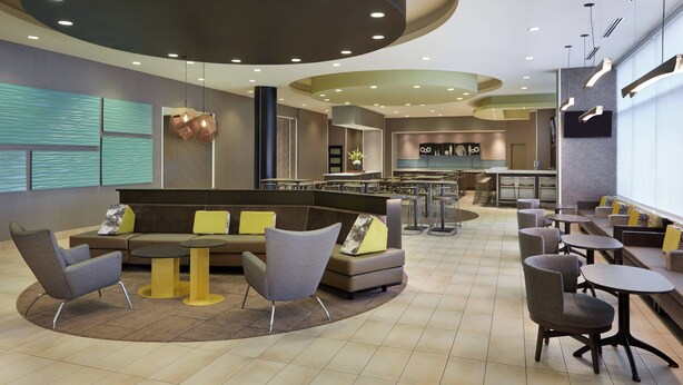 A modern lounge area with seating arrangements, a kitchen in the background, and a large window providing natural light. - SpringHill Suites by Marriott Toronto Vaughan (Vaughan)