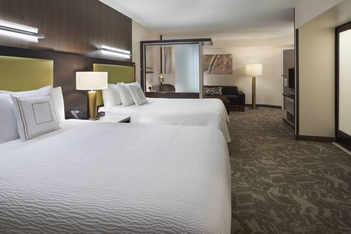 A hotel room with two beds, a desk, a chair, a mirror, a TV, and a carpeted floor.