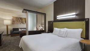 A hotel room with a large bed, a bedside table, a lamp, a sofa, and a mirror. - SpringHill Suites by Marriott Toronto Vaughan (Vaughan)