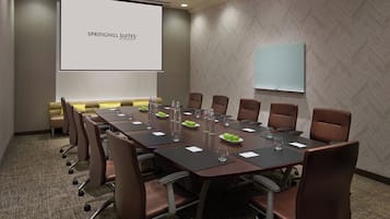 Un salón de conferencias con una larga mesa, sillas marrones y una pantalla de proyector que muestra "SPRINGHILL SUITES BY MARSHOTT".