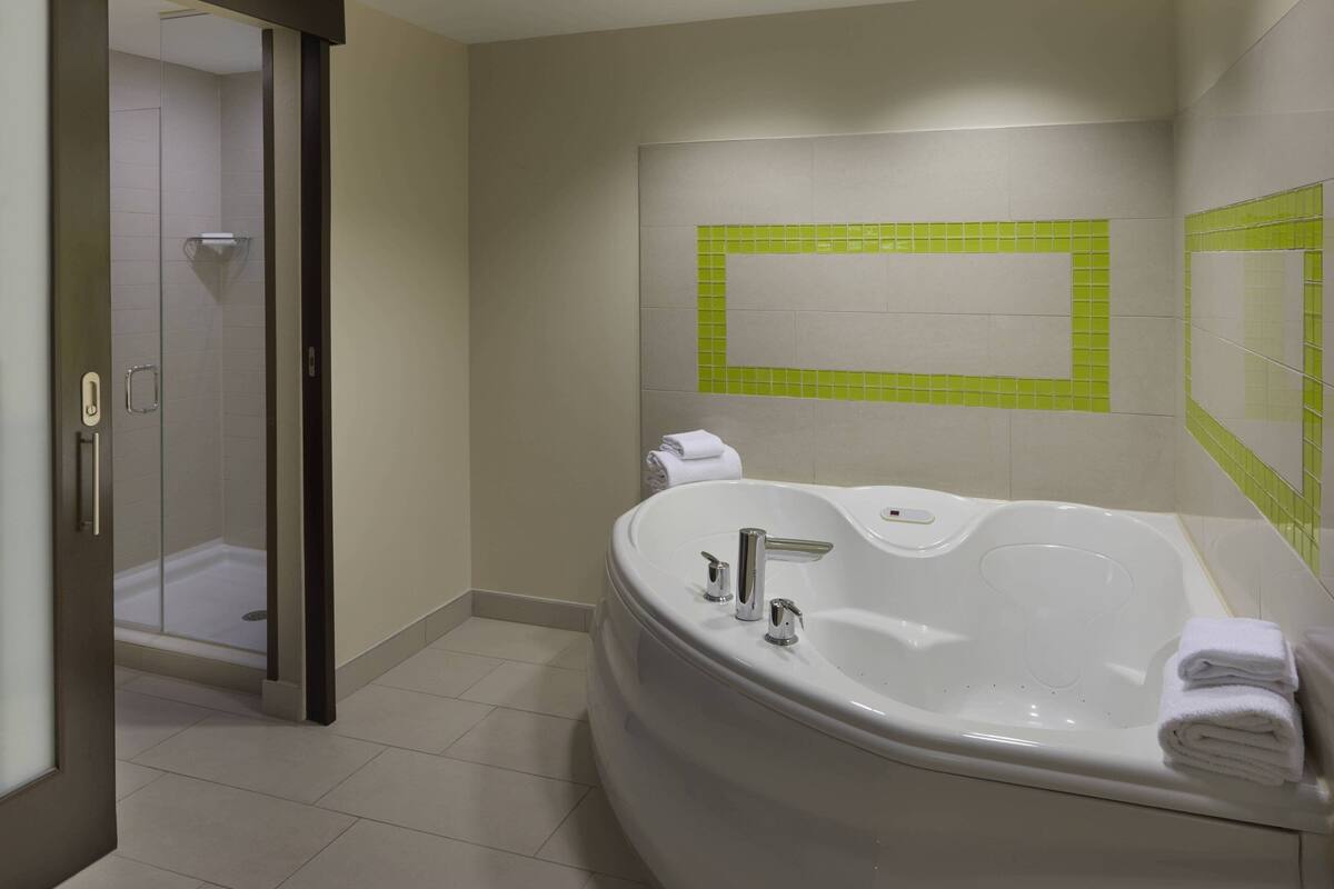 A modern bathroom with a large bathtub, a shower area, and a mirror with green-tiled accent.