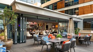 An outdoor seating area with tables and chairs, a bar in the background, and a large potted plant. - Harbour Hotel Guildford (Guildford)