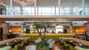 A spacious lobby with a high ceiling, a central seating area with a tree, and a bar in the background. - Harbour Hotel Guildford (Guildford)