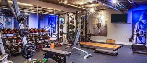 A gym with weightlifting equipment, treadmills, and a wall-mounted TV.