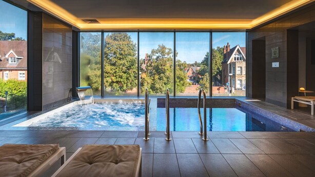 A modern indoor pool area with a view of the surrounding neighborhood, including trees and buildings. - Harbour Hotel Guildford (Guildford)