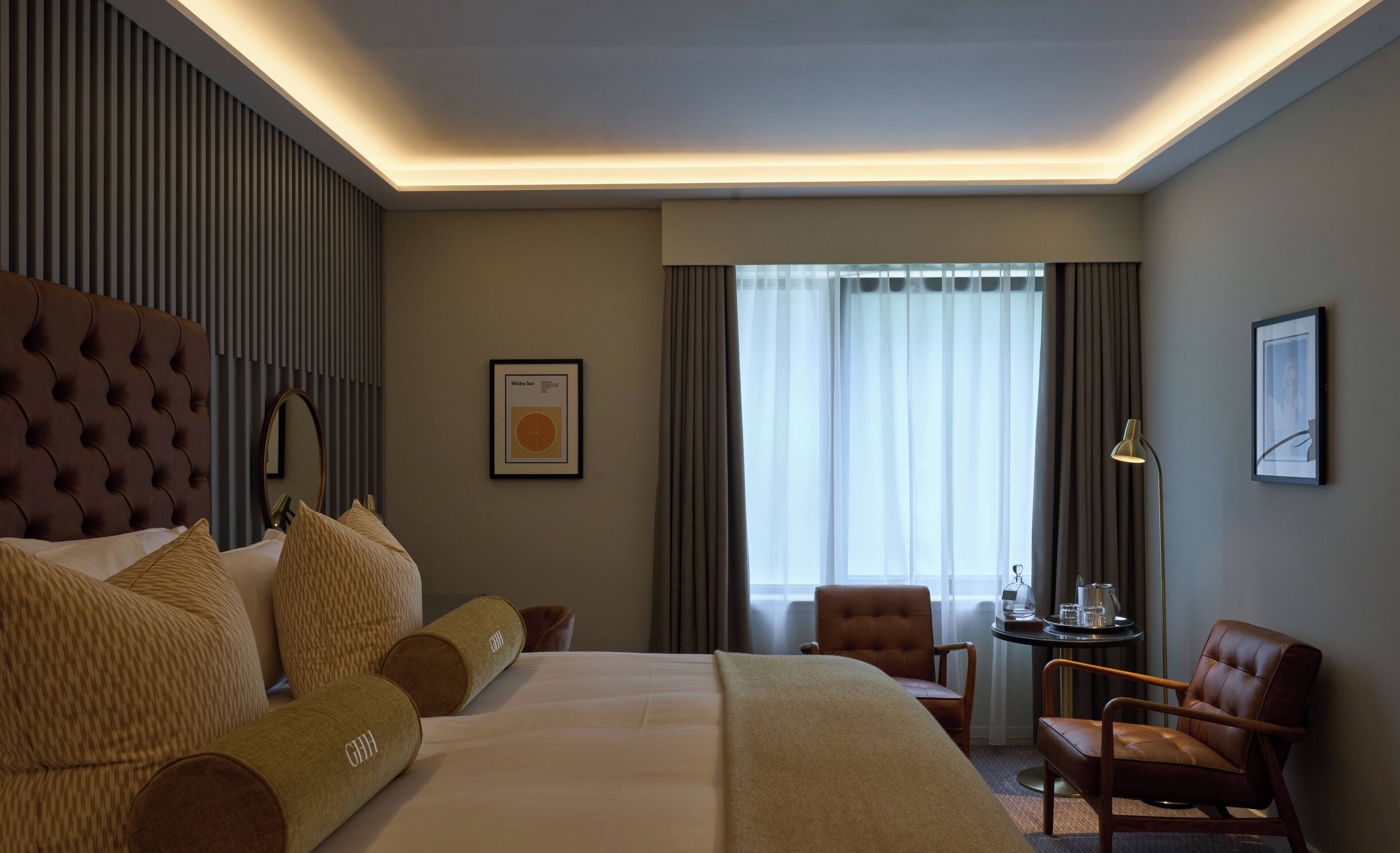 A hotel room with a large bed, a headboard, a desk with a chair, a window with curtains, and a framed picture on the wall.