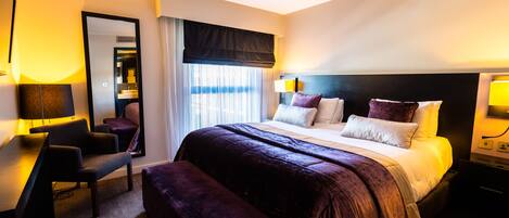 A hotel room with a large bed, a desk, a chair, and a mirror.