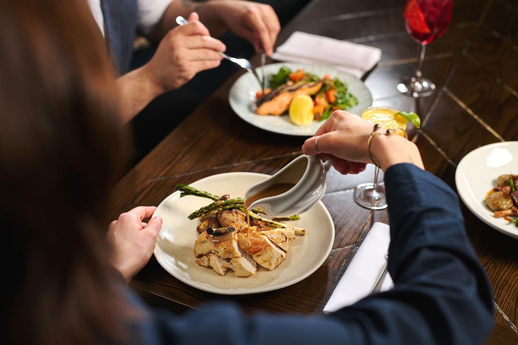 A person dining at a restaurant with a plate of food and a glass of red wine.