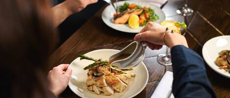 A person dining at a restaurant with a plate of food and a glass of red wine.