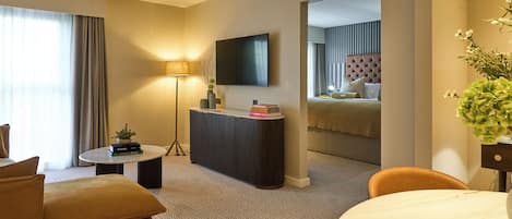 Une chambre d’hôtel avec un canapé, une petite table, une lampe, une télévision et un miroir qui reflète le lit.