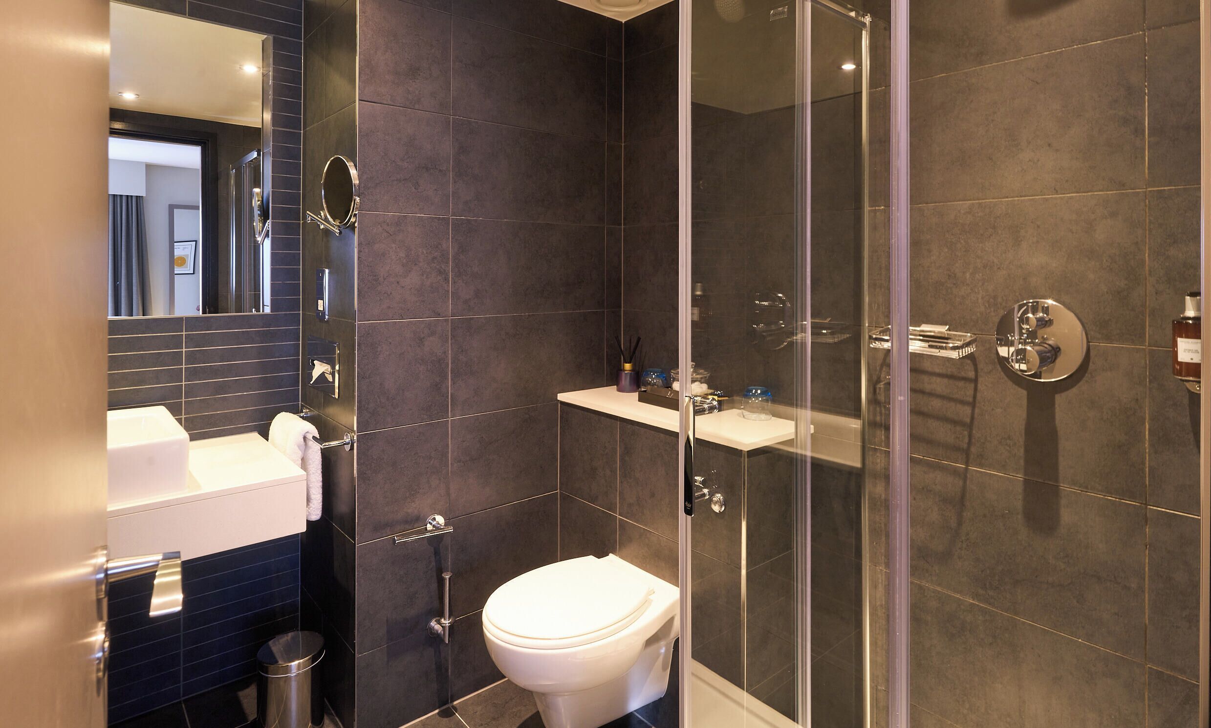 Un baño moderno con cabina de ducha de vidrio, inodoro blanco y tocador con espejo.