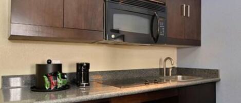 A compact kitchen with dark wooden cabinets, a built-in microwave, a sink, and a dishwasher.