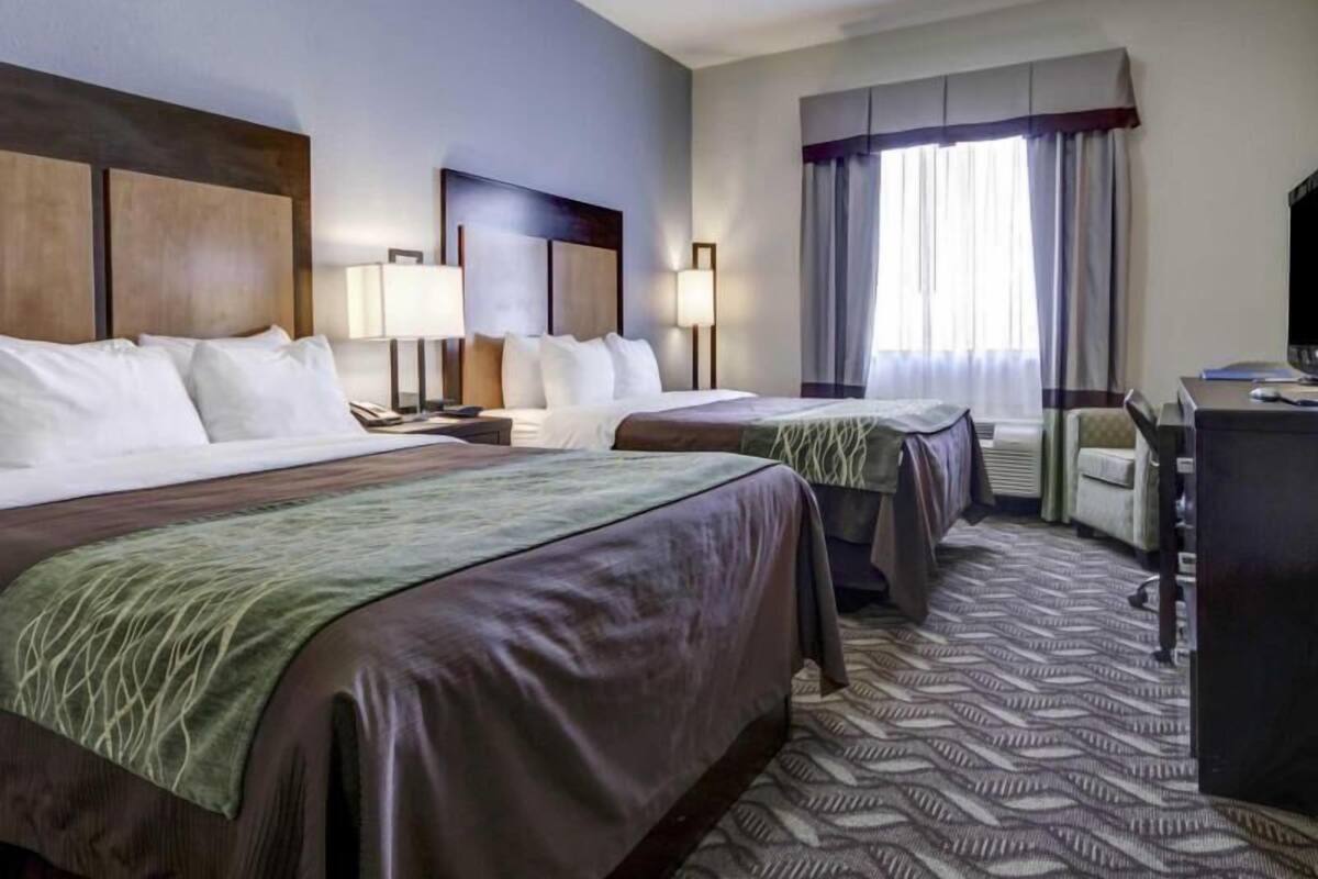 A hotel room with two beds, a desk, a chair, a television, and a window with curtains.