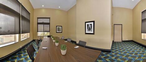 A conference room with a long table, chairs, potted plants, framed pictures, and a patterned carpet.