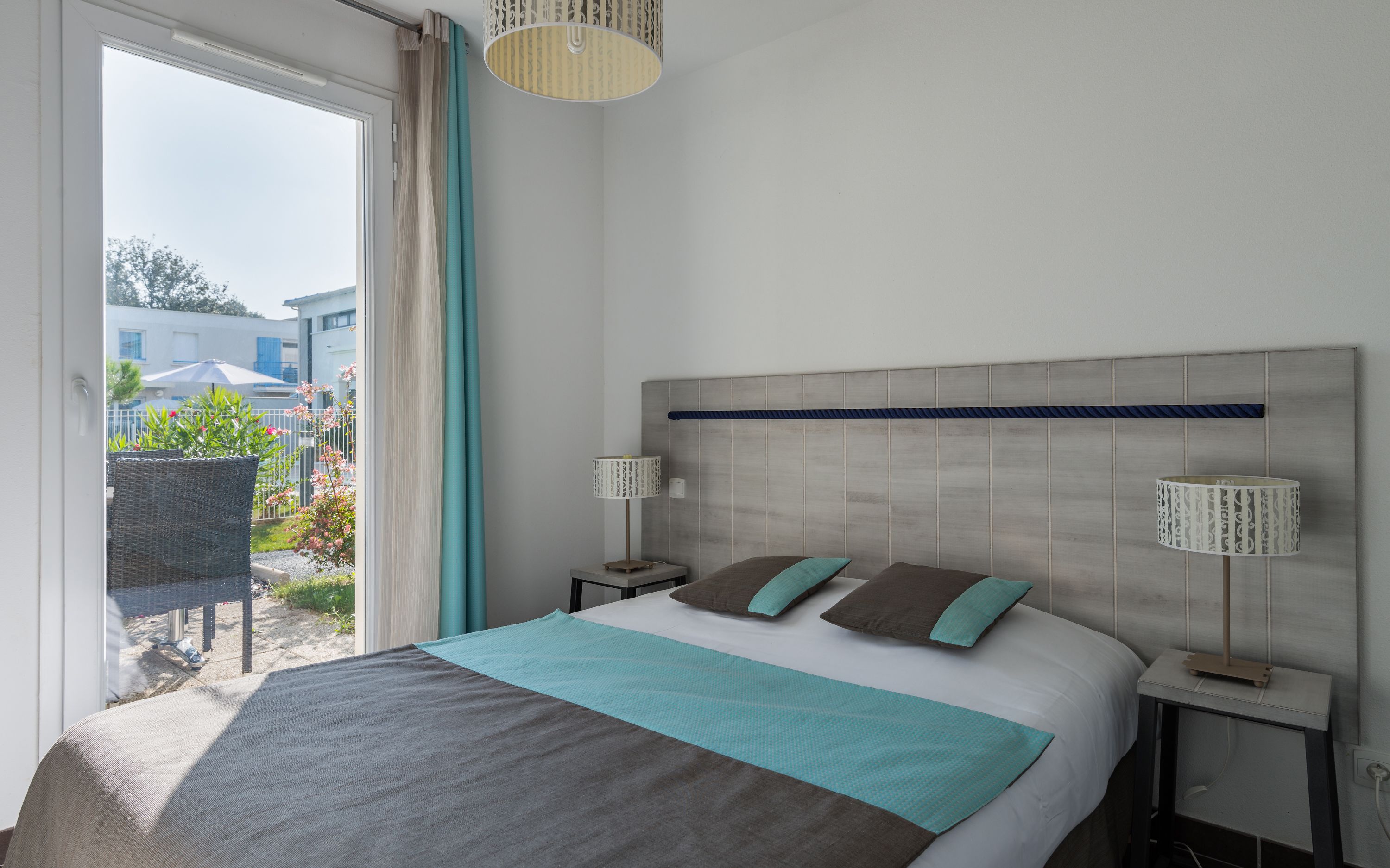 A bedroom with a bed, two bedside tables, a headboard, and a view of the outside.