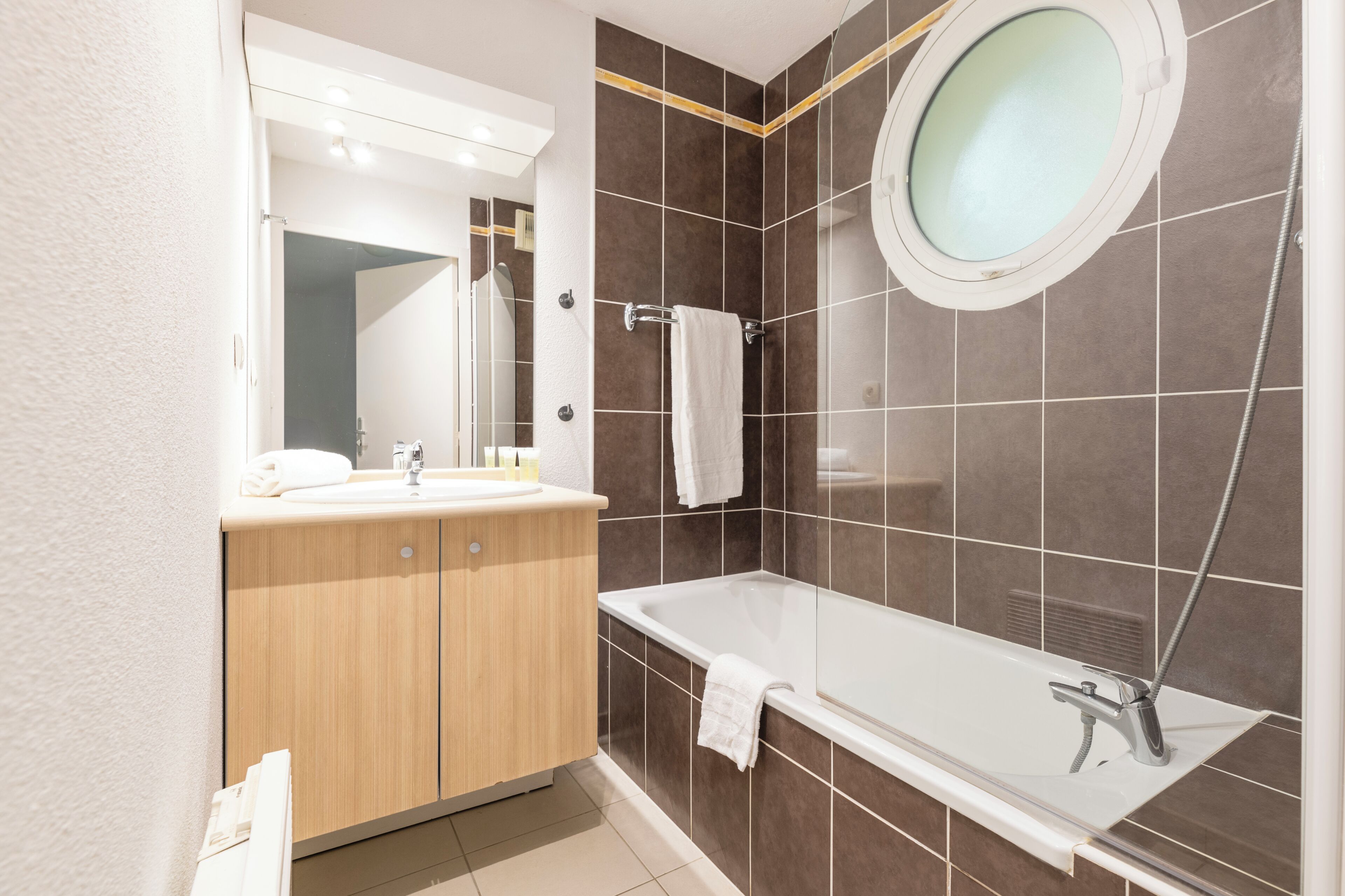 Een moderne badkamer met een houten wastafelmeubel, een grote spiegel, een badkuip en een douchehoek.