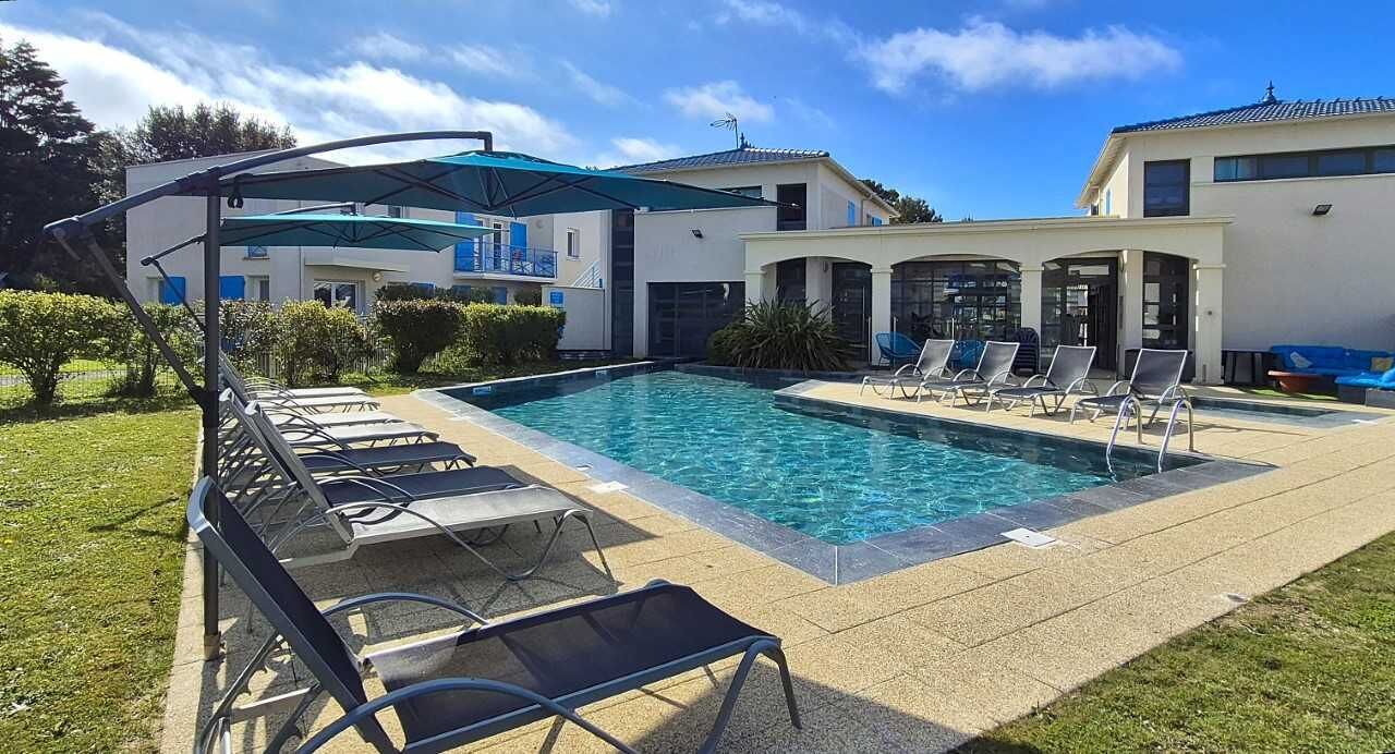 A swimming pool with lounge chairs, a covered seating area, and a building with a modern design.