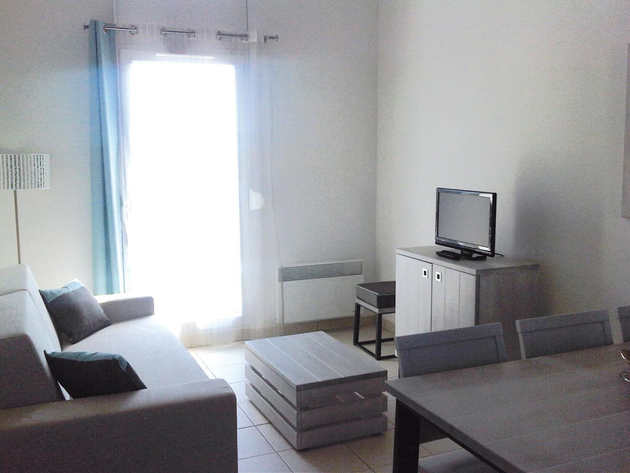 A modern living room with a sofa, a coffee table, a TV on a cabinet, and a dining table with chairs.