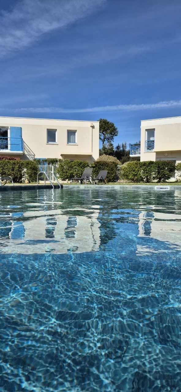 A clear swimming pool with a reflection, surrounded by modern buildings and greenery.