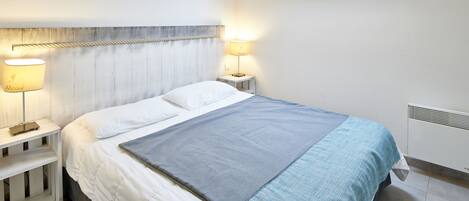 A bedroom with a bed, two bedside tables with lamps, a skylight, and a radiator.