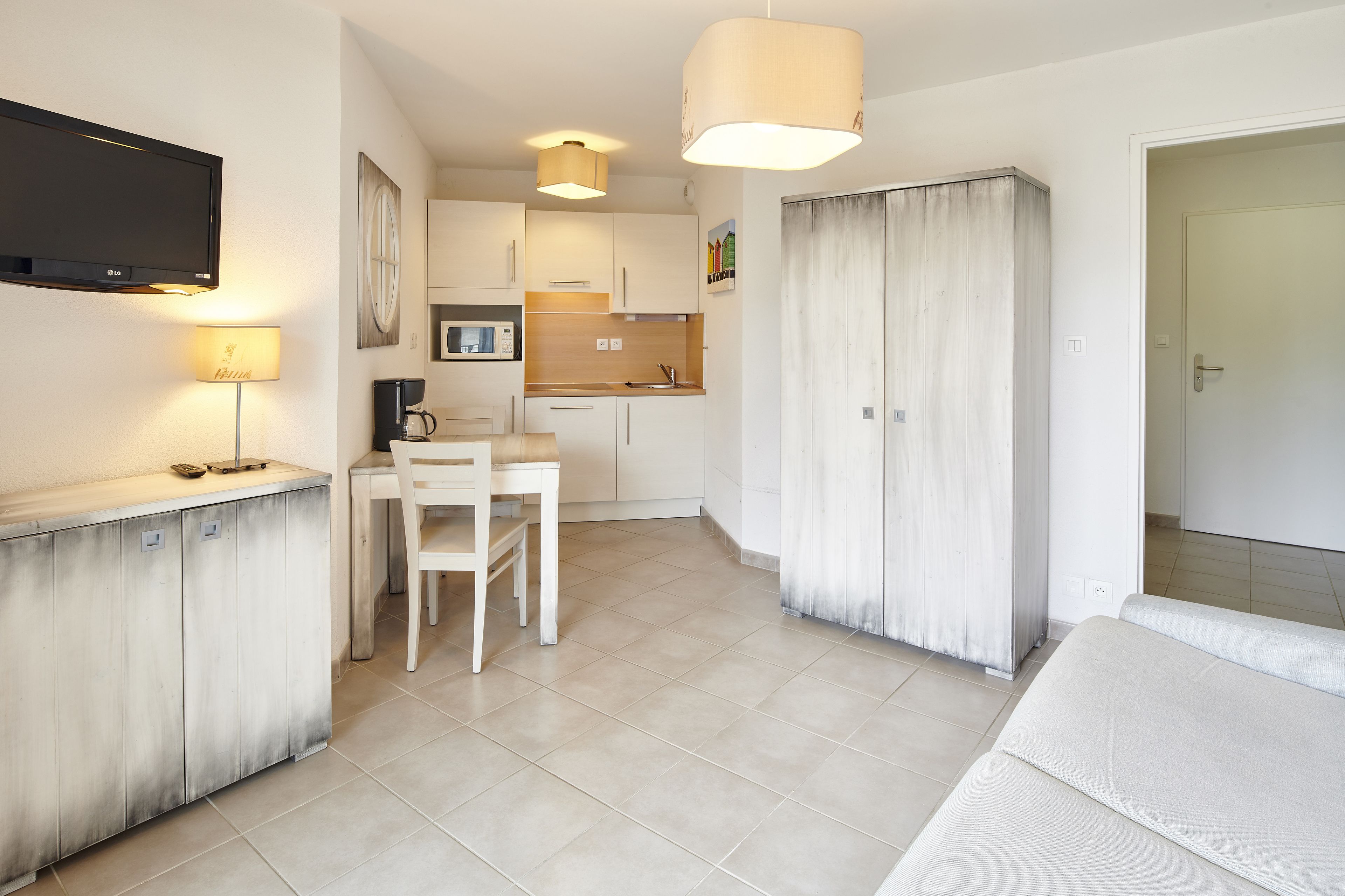 A modern kitchen with white cabinets, a dining table, and a TV mounted on the wall.