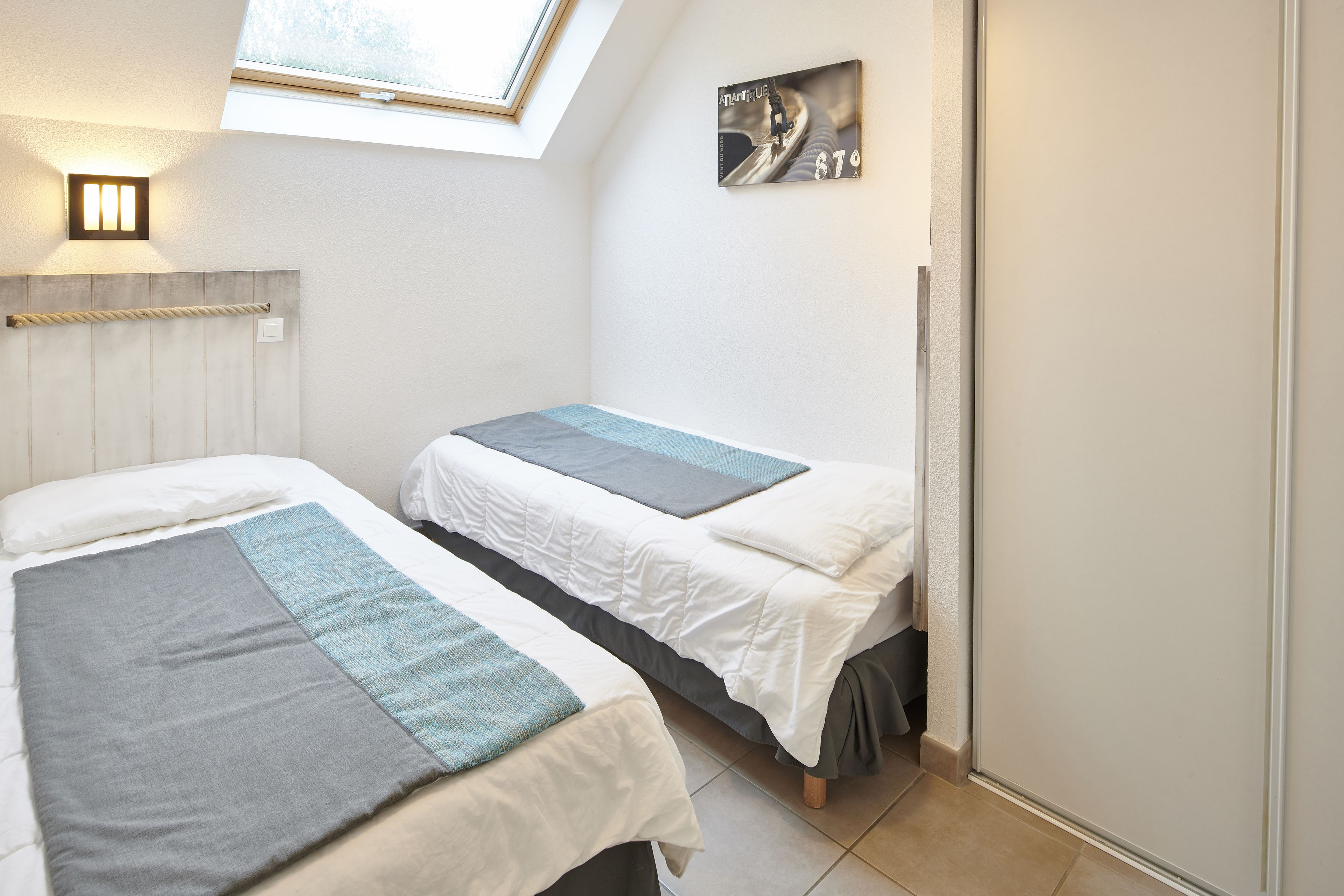 A bedroom with two beds, a skylight, a wall-mounted light, and a framed picture.