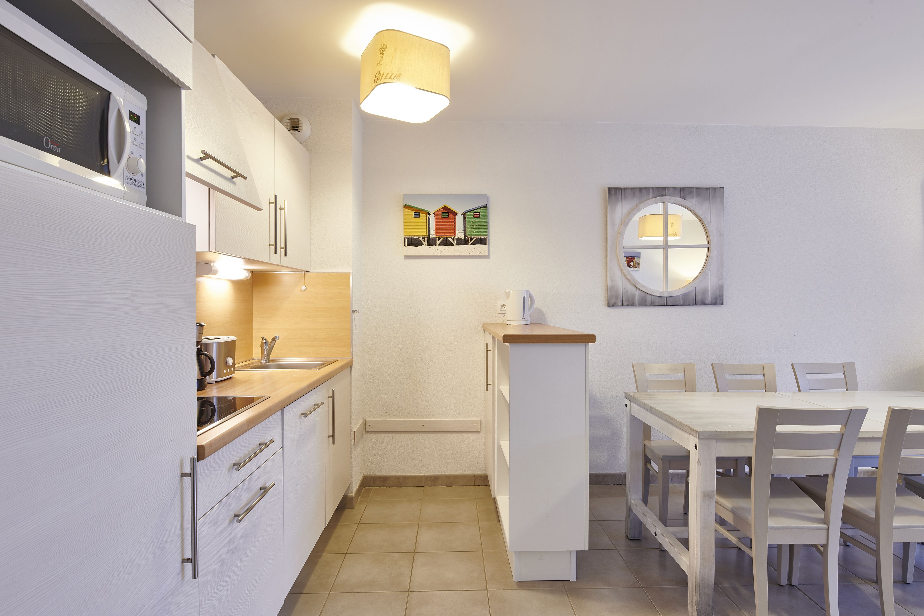 A modern kitchen with white cabinets, a built-in microwave, a wooden countertop, and a dining area with a white table and chairs.
