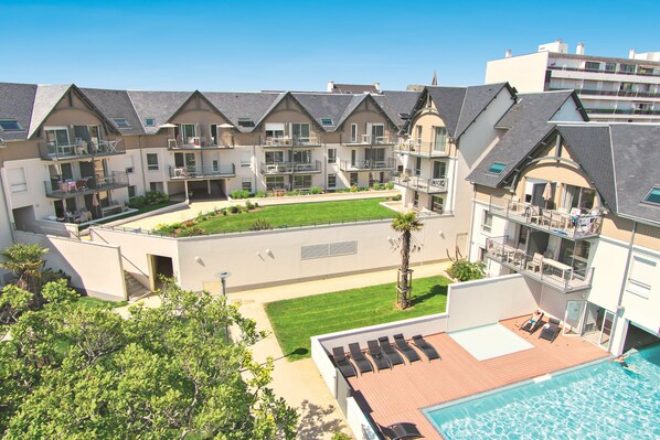 A multi-story hotel with balconies, a swimming pool, and a well-maintained lawn.
