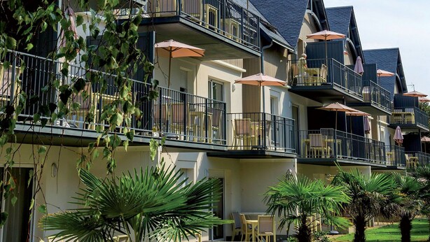 Un hotel de varios pisos con balcones, mobiliario exterior y palmeras.